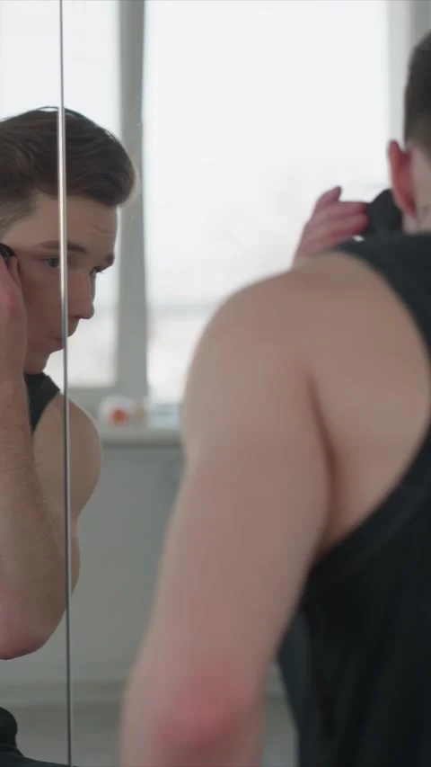 Young man with tattoos performing shaving routine in front of mirror indoors Stock Footage 343085670