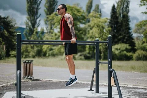 Young man with tattoos training on parallel bars at an outdoor fitness park Stock Photos