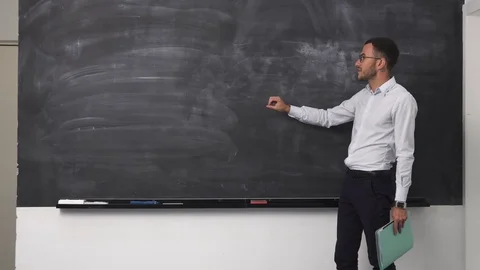 Young man teacher explaining something at clean blackboard Stock Footage 77161020