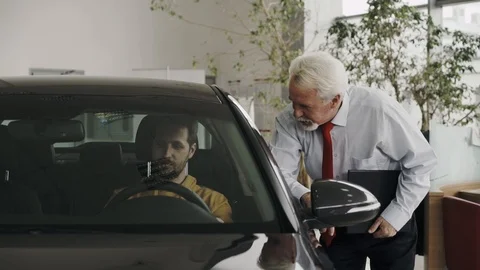 Young man is testing the car at the auto salon with the help of sales assistant Stock Footage 93083888