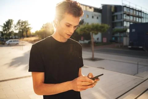Young man text messaging on mobile phone while walking on sidewalk in city Stock Photos