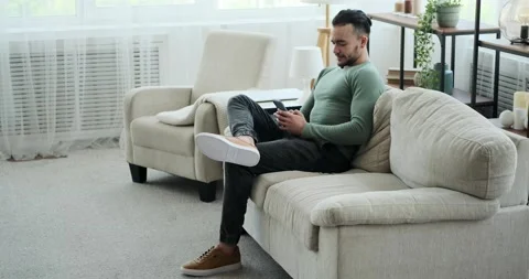 Young man text messaging using mobile phone while sitting on sofa Stock Footage 156543528