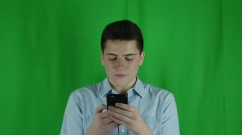 Young man is texting and smiles in front of greenscreen Vidéo 59090404