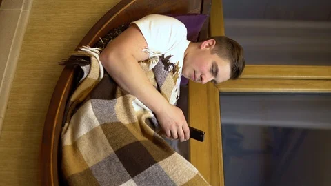 A young man is texting on the phone. A man lies on a window sill by the window Stock-Footage 126392494