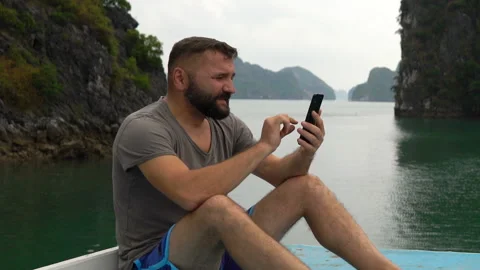Young man texting on smartphone, sitting on boat deck Stock Footage 163342287