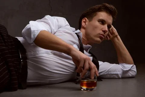 A young man is thinking about something drinking whiskey lying on the floor Stock Photos