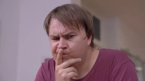 Young man is thinking hard about problem, putting hand to his face and squinting Stock Footage 147859621
