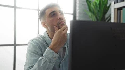 Young man thinking in modern office, pondering at computer with green plant.. Stock Footage 305543744