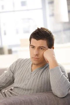 Young man thinking on sofa Goodlooking young man sitting on sofa in living... Stock Photos