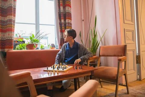 Young man thinking while playing chess alone in a cozy living room Stock Photos