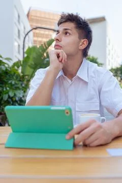 Young man thinking while using tablet at outdoor cafe in vertical urban setting Stock Photos