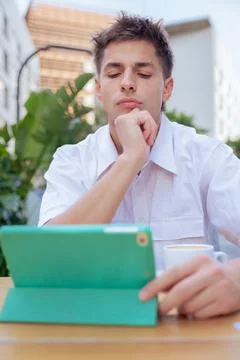 Young man thinking while using tablet at outdoor cafe in vertical urban setting Stock Photos