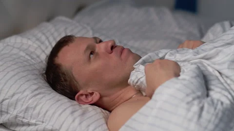 Young man thinks before going to bed lying in bed, suffers from insomnia Stock Footage 130879557