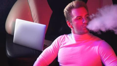Young man thinks smokes a hookah and looks into the distance at home with a l Stock Photos