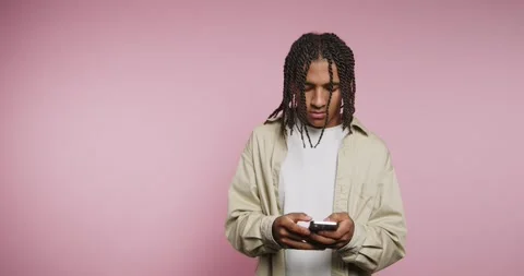 Young man thinks while holding a phone against a pink background Vídeos de archivo 326787994