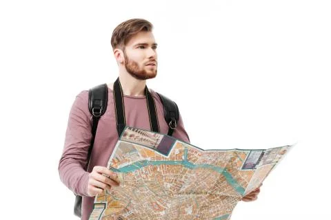 Young man thoughtfully looking aside with open map in hands and backpack on 스톡 사진