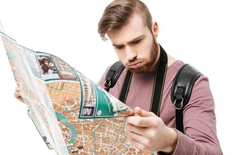 Young man thoughtfully looking in map in hands with backpack on white background Foto stock