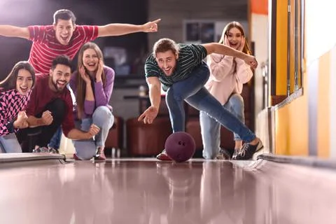 Young man throwing ball and spending time with friends in bowling club Stock Photos