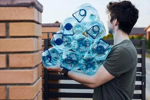 Young man throwing out empty used plastic water bottles into trash bin Stock Photos