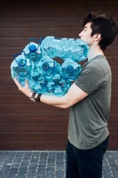 Young man throwing out empty used plastic water bottles into trash bin Stock Photos