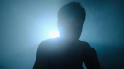 Young man throwing punch into camera in dark cinematic lighting, silhouette Stock Footage 312111415