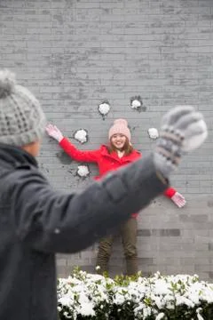 Young man throwing snow balls at young woman on wall Stock Photos