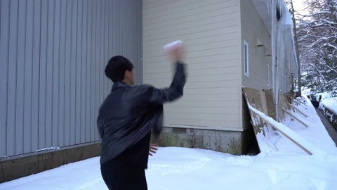 Young Man Throwing Snowball At Large Icicles Hanging From Building Stock Footage 101011390