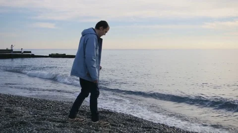 Young man throwing stones into the ocean Stock Footage 71618599