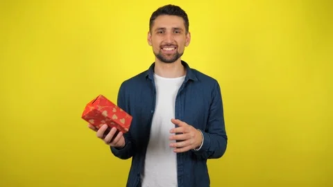 A young man throws a box with a gift from hand to hand and smiles Stock Footage 119862177