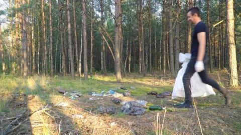 Young man throws garbage out of bag in forest Stock Footage 118087125