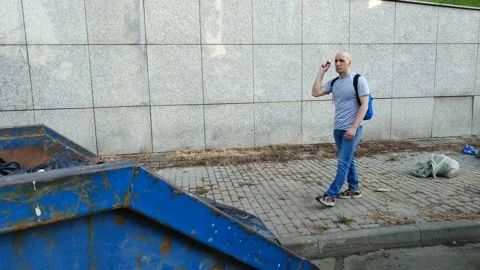 Young man throws small garbage into large dumpster Stock Footage 201167340