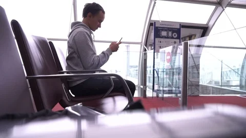 Young man is thumbng a text message while sitting in airport. Stock Footage 88154210