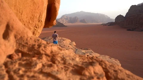 Young man is to the top of cliff. Wadi Rum also known as The Valley Stock Footage 126784343