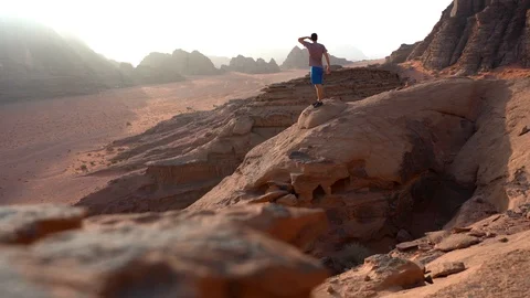 Young man is to the top of cliff. Wadi Rum also known as The Valley Stock Footage 126786016