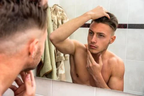 Young man touching his face while looking in mirror Stock Photos