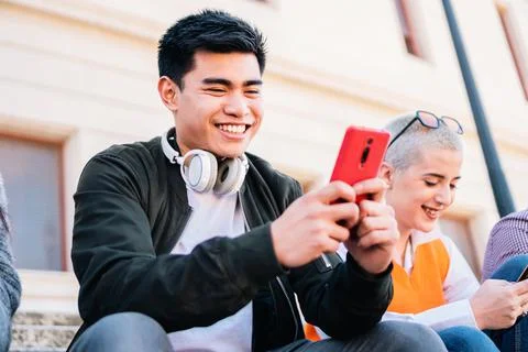 Young man touching a mobile screen sitting outdoor and smiling. Stock Photos