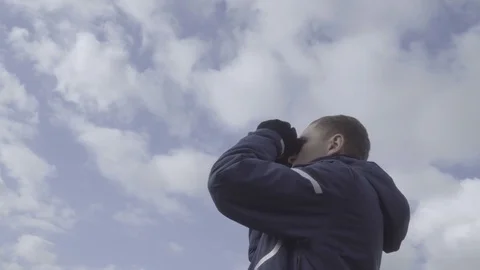 Young man tourist looking through binoculars. Sky clouds background 4k Stock Footage 85121744