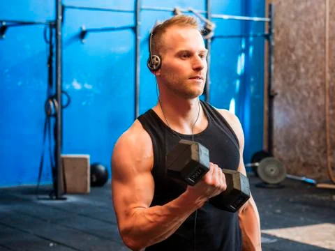 Young man training biceps lifting dumbbells Stock Photos