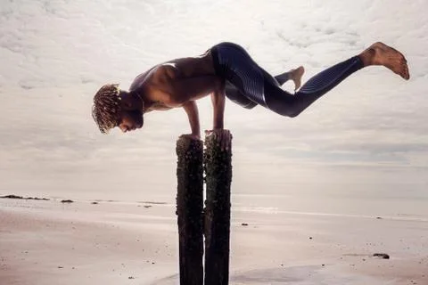 Young man training, doing handstand on wooden beach posts Stock Photos