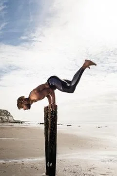 Young man training, doing handstand with raised legs on wooden beach posts Stock Photos