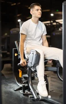 Young man training on hip abduction machine at gym Stock Photos