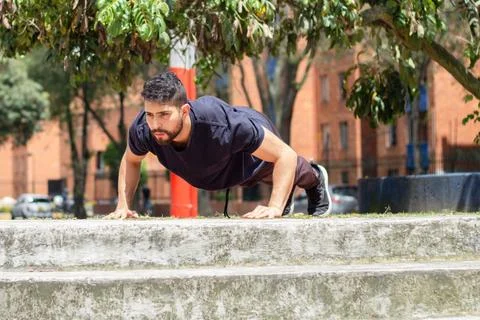 Young man training push ups on a chair in an outdoor park in the city Stock Photos