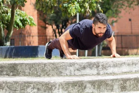 Young man training push ups on a chair in an outdoor park in the city Stock Photos