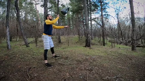 A young man trains with a kettlebell in the forest. Kettlebell juggling. Stock Footage 151167767