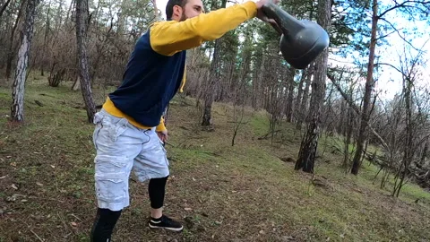 A young man trains with a kettlebell in the forest. Kettlebell juggling. Stock Footage 151168381