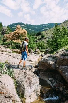 Young man traveler walking alone by a mountain river with rocky summer landscape Stock Photos