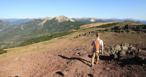 Young man trekking down a volcano. Background of woods and andes mountain chain 스톡 동영상 126731073