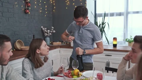 A young man tries a wine bottle with a corkscrew and breaks it. Guests sit near Stock Footage 144471069