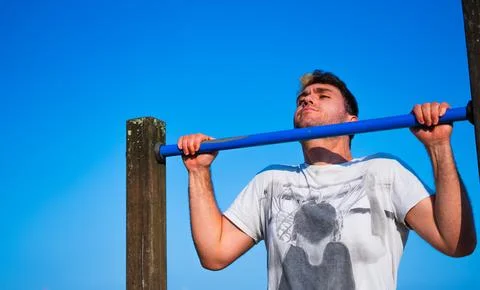 Young man trying to do pullups in foreground Stock Photos