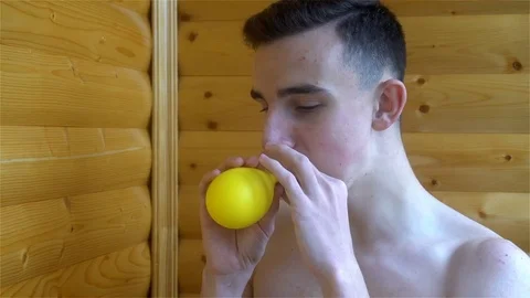 Young man trying to inflate a yellow balloon Stock Footage 82124248
